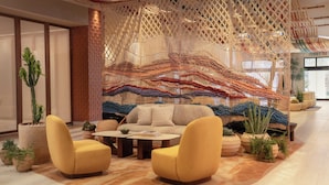 A modern living room with a sofa, two armchairs, a coffee table, and a decorative macrame wall. - Kimpton Miralina Resort & Villas by IHG (Paradise Valley)