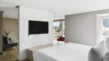 Una habitación de hotel moderna con una cama grande, un televisor de pantalla plana montado en la pared, una silla roja y vistas a la ciudad a través de amplias ventanas.