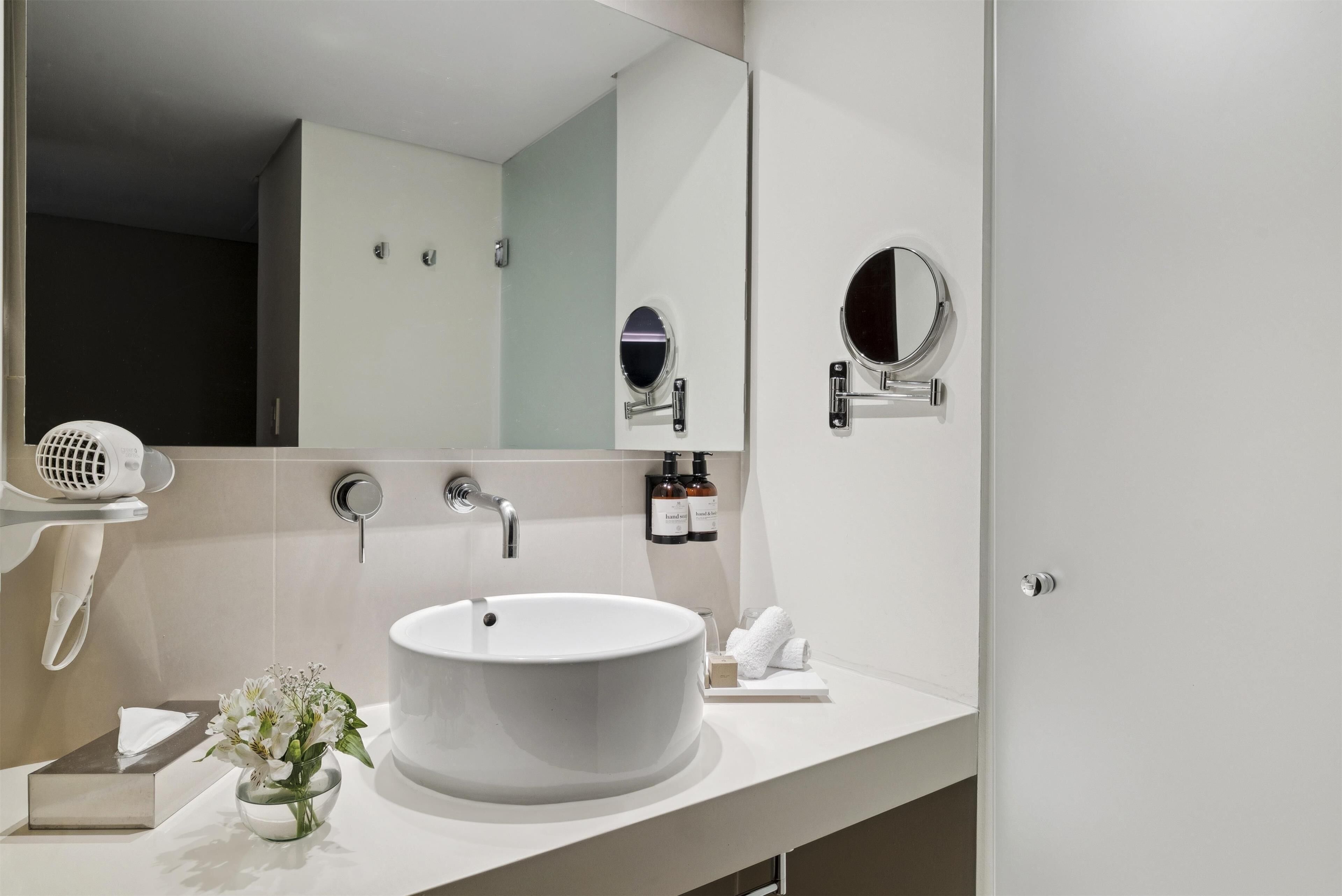 Ein modernes Badezimmer mit einem großen Waschbecken, einem Spiegel und einem Fön auf einem Regal.