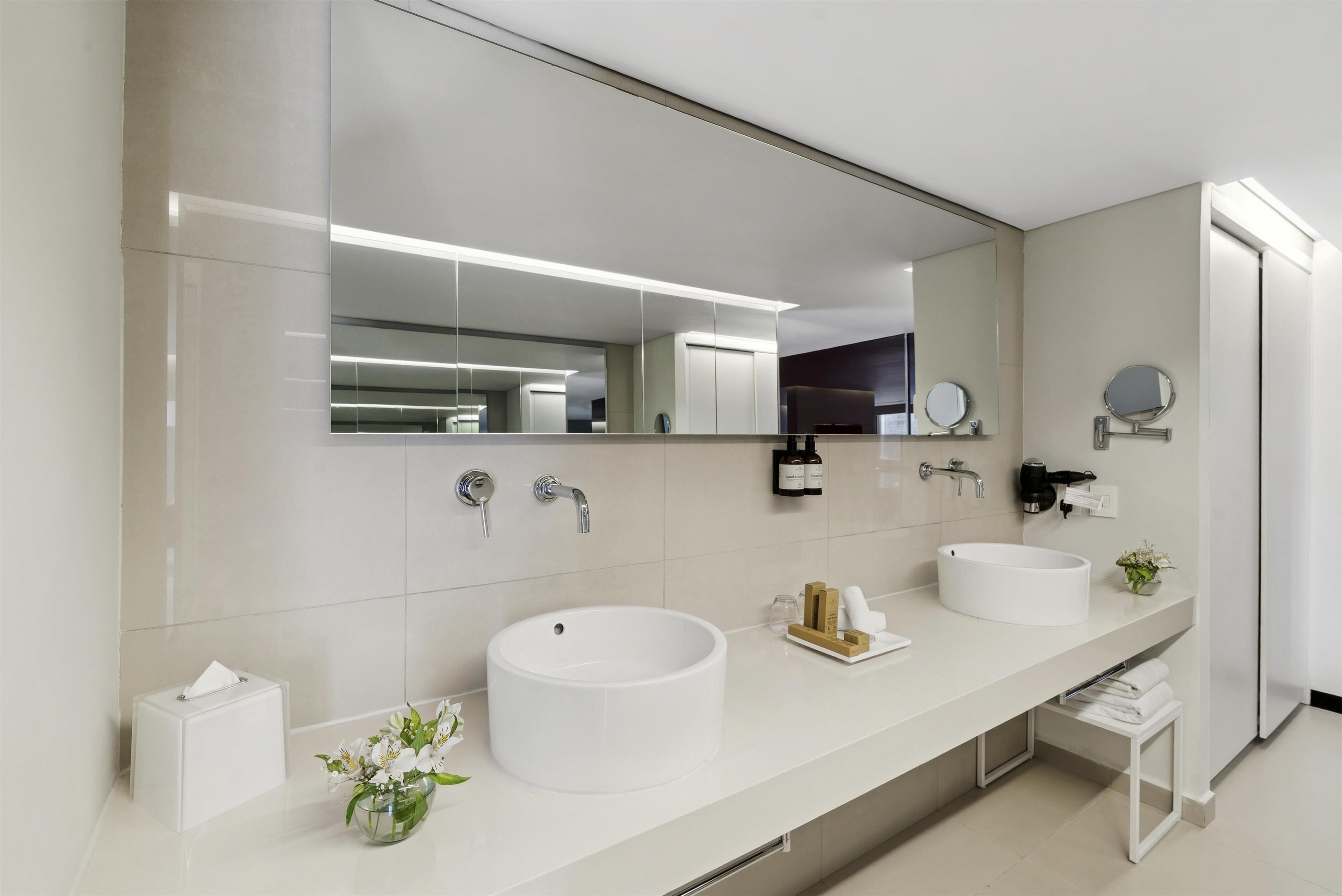 Une salle de bain moderne avec deux lavabos, un grand miroir et un porte-serviettes.