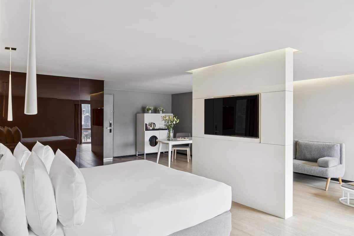Ett modernt hotellrum med en stor säng, ett skrivbord och en tv som är monterad på väggen.