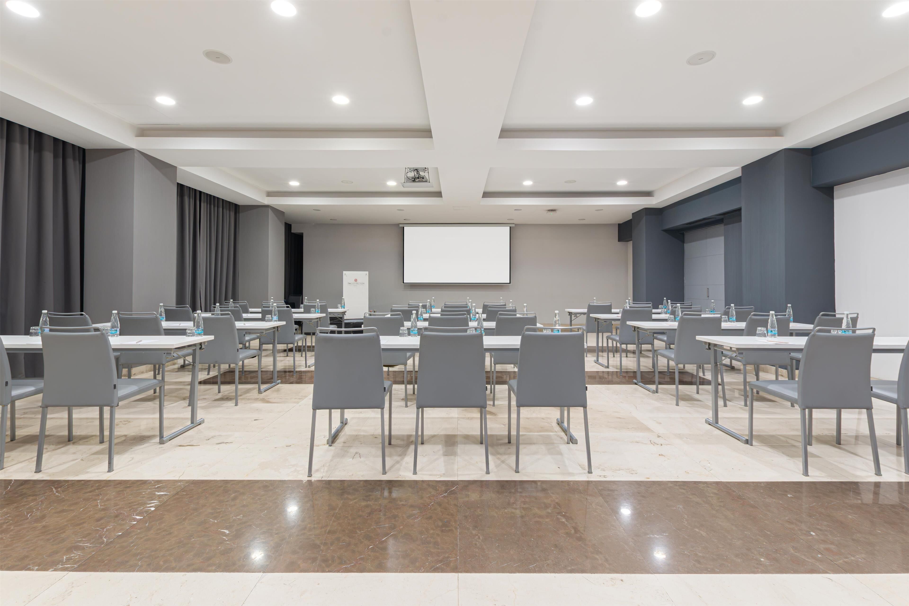 A conference room with multiple tables and chairs, a projector screen, and a whiteboard.