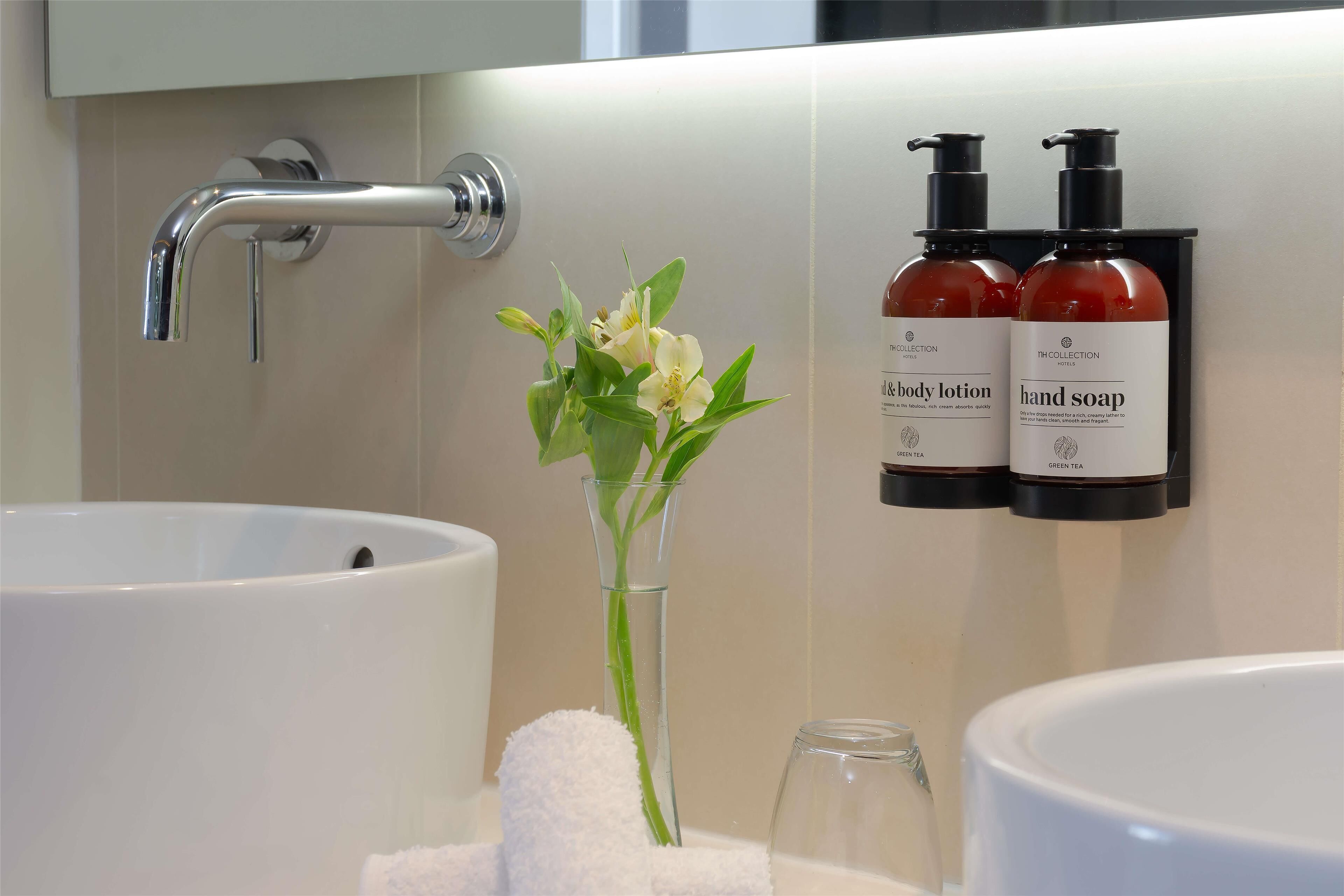 A bathroom with a white sink, a glass vase with flowers, and two bottles of hand soap and body lotion.