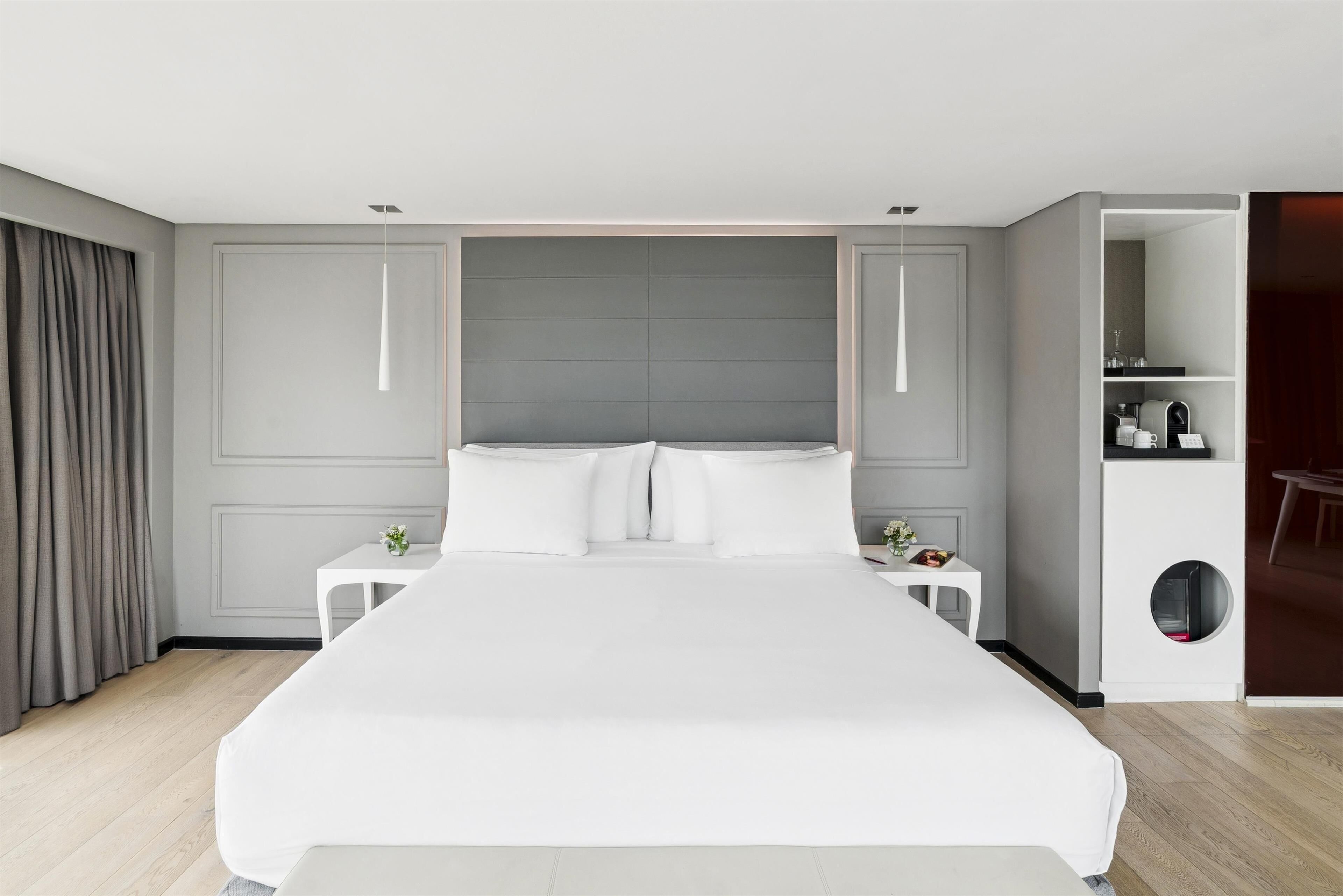 A modern hotel room with a large bed, bedside tables, a small desk, and a built-in shelf with toiletries.