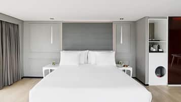 A modern hotel room with a large bed, bedside tables, a small desk, and a built-in shelf with toiletries.
