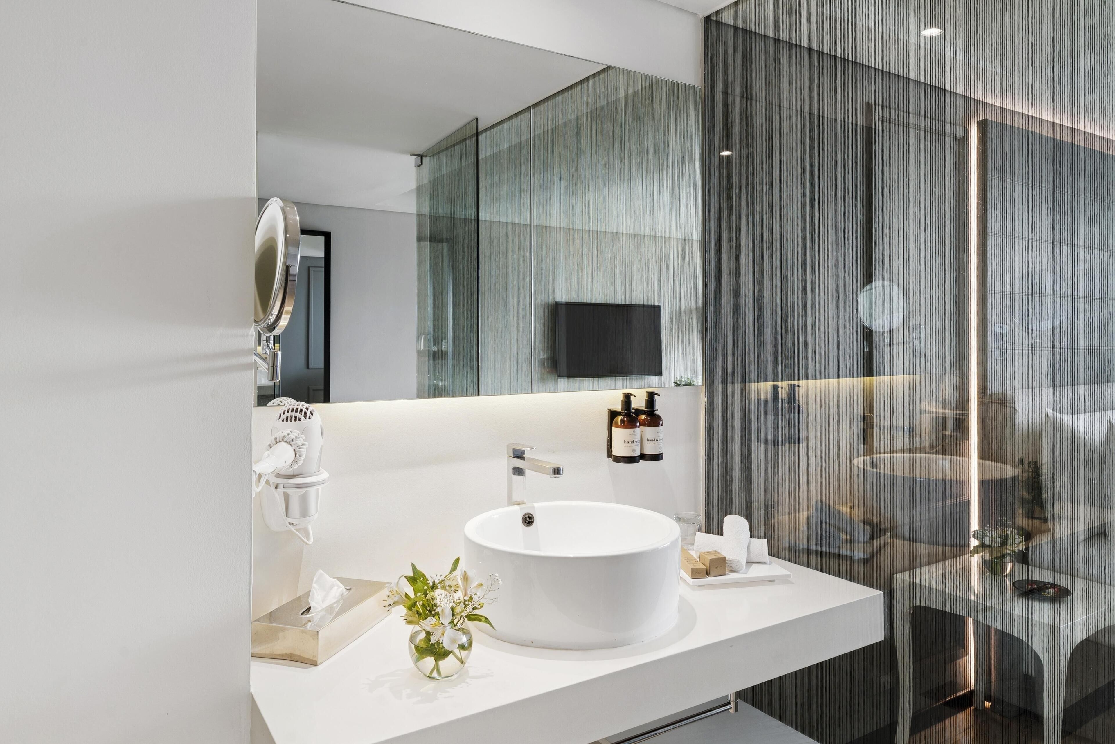 Un baño moderno con un espejo grande, un lavamanos redondo y una cabina de ducha de vidrio.