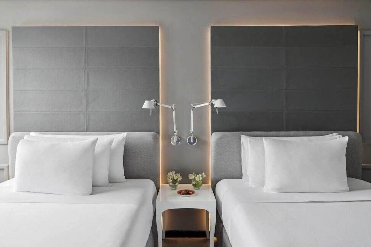 A hotel room with two beds, a nightstand with a lamp, and a wall-mounted light fixture.