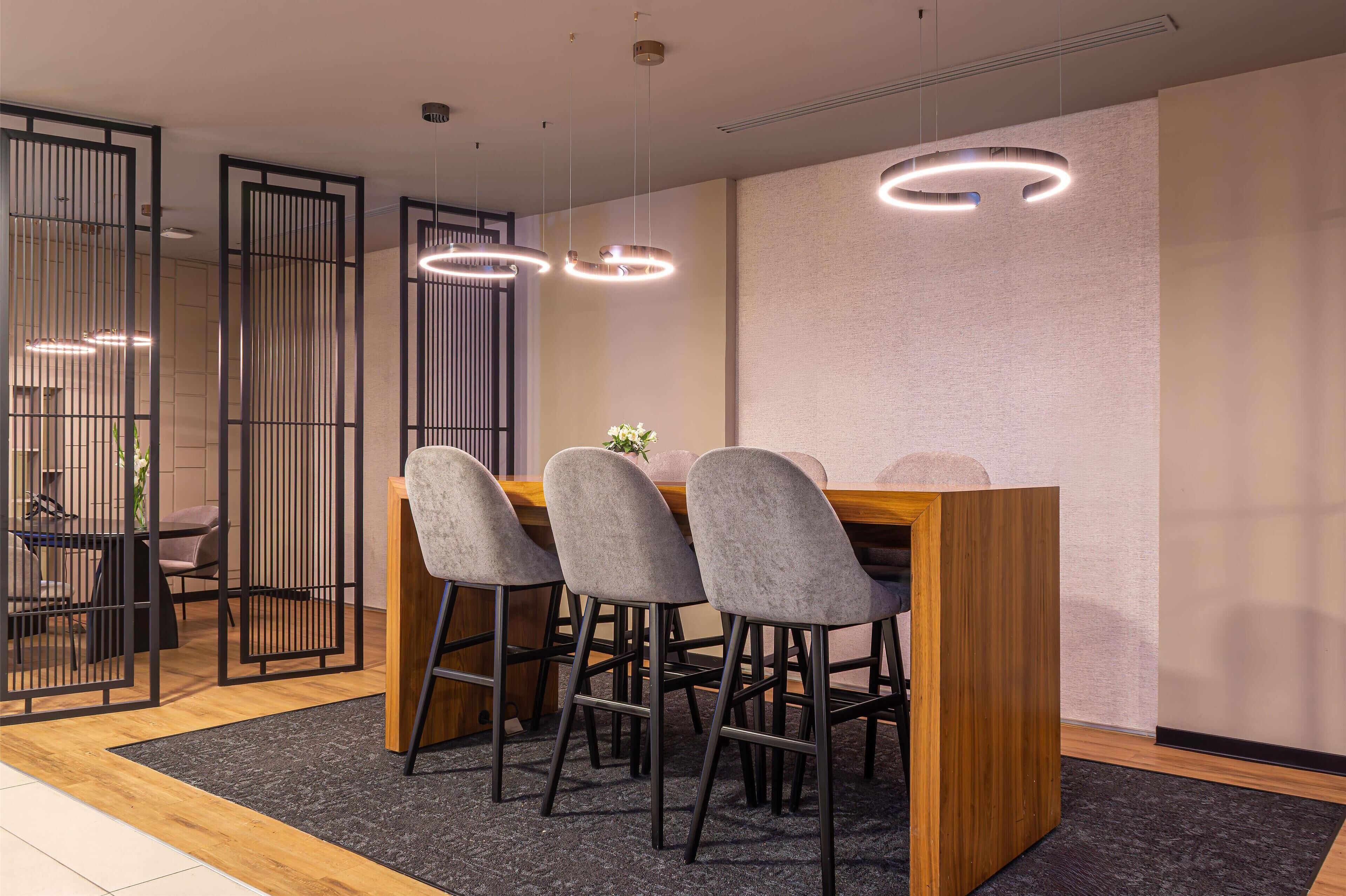 A modern dining area with a wooden table, four grey chairs, and pendant lighting.