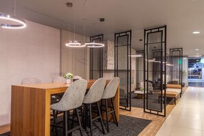A modern dining area with a wooden table and grey upholstered chairs, surrounded by black partitions and pendant lighting.