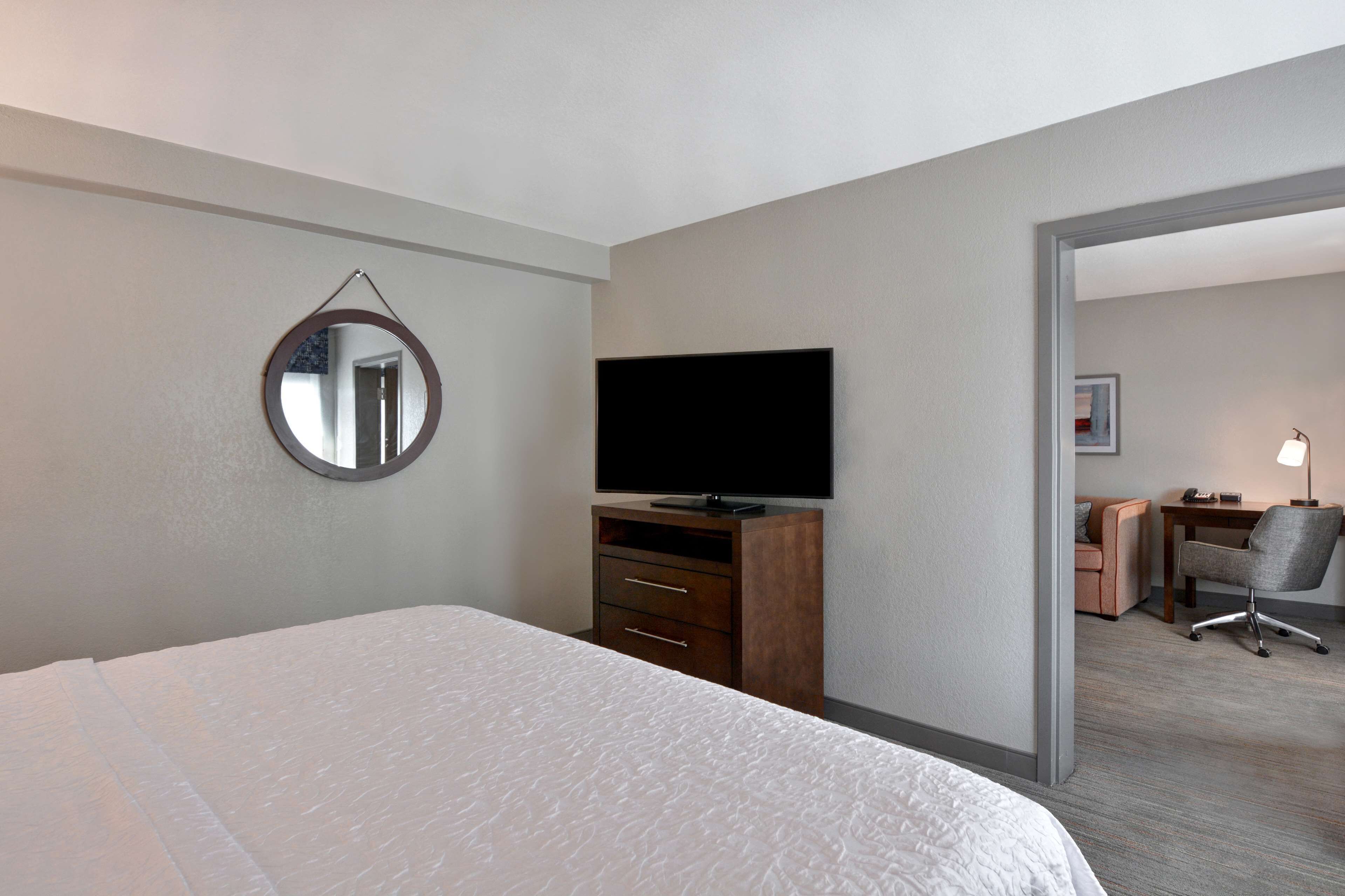 A hotel room with a bed, a TV, a desk with a chair, and a mirror on the wall.