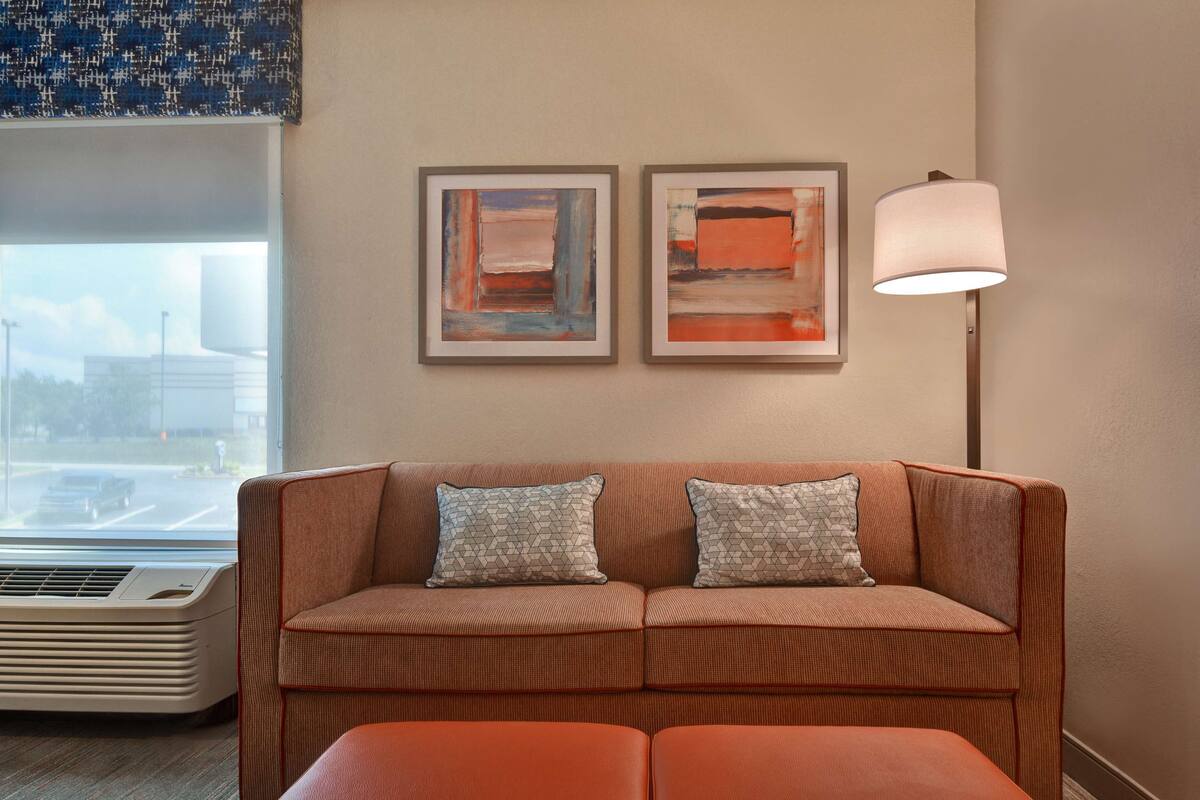 A living room with a sofa, two pillows, a floor lamp, and two framed abstract paintings on the wall.