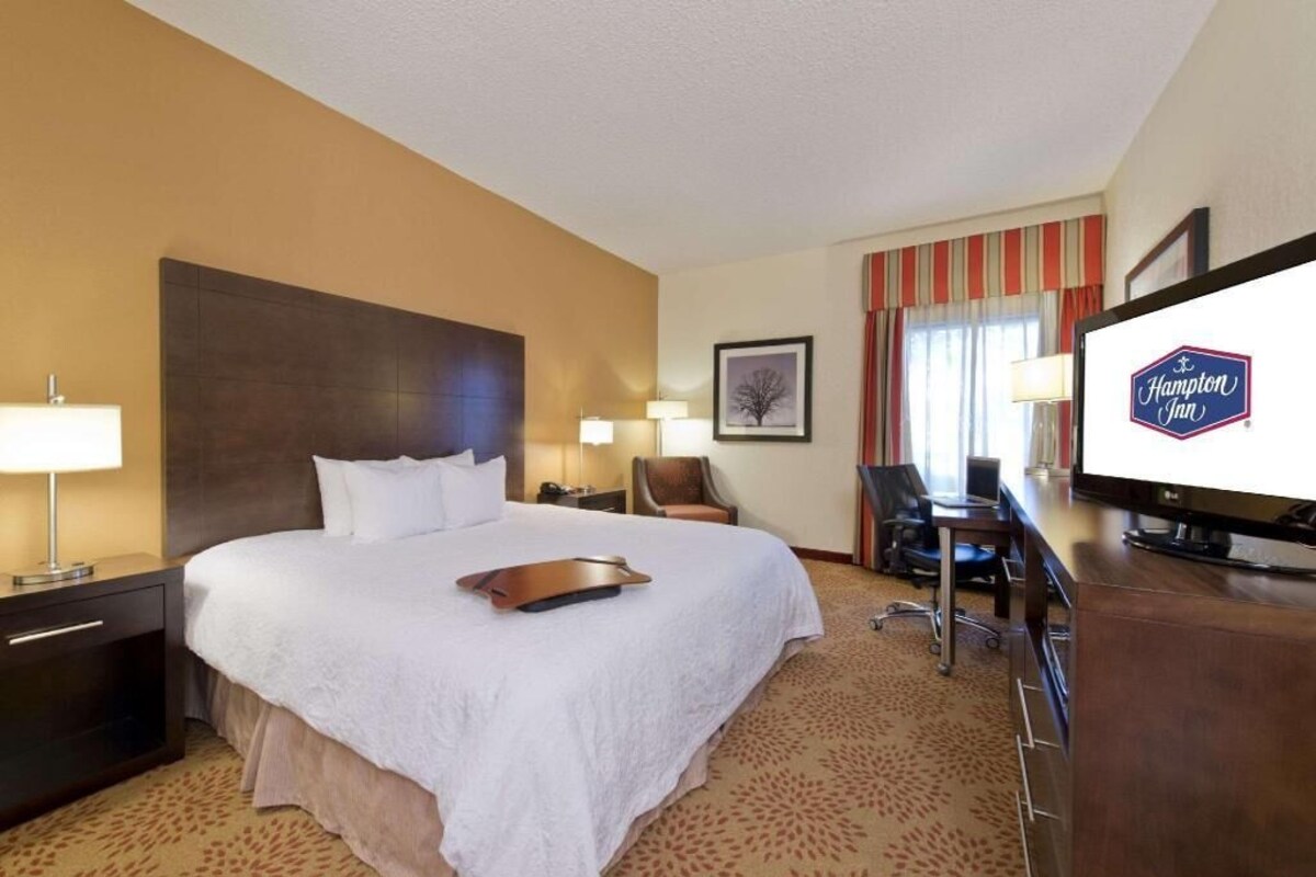 Habitación de hotel con cama, escritorio, silla, televisor y un letrero de Hampton Inn.