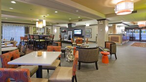 Un hall d’hôtel doté de plusieurs espaces aménagés avec des sièges, d’un comptoir de réception et d’un écran de télévision.