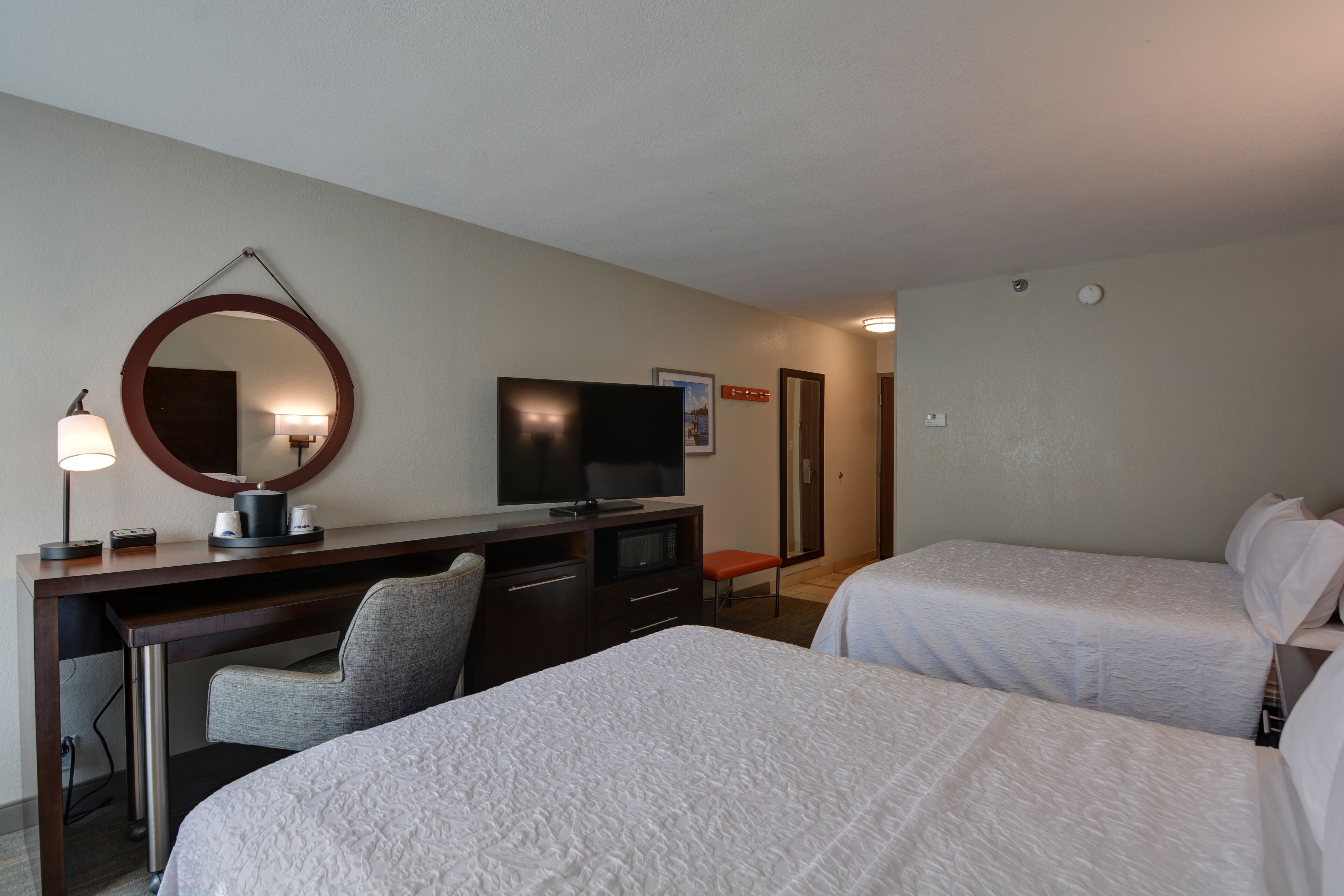 A hotel room with two beds, a desk with a computer, a television, and a mirror.