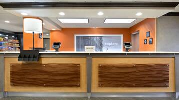 A hotel reception desk with a modern design, a digital kiosk, and a sign that reads "Hilton explore."