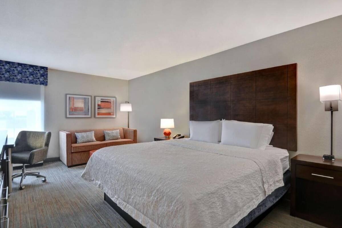 A hotel room with a large bed, a desk, a chair, a sofa, and two bedside lamps.