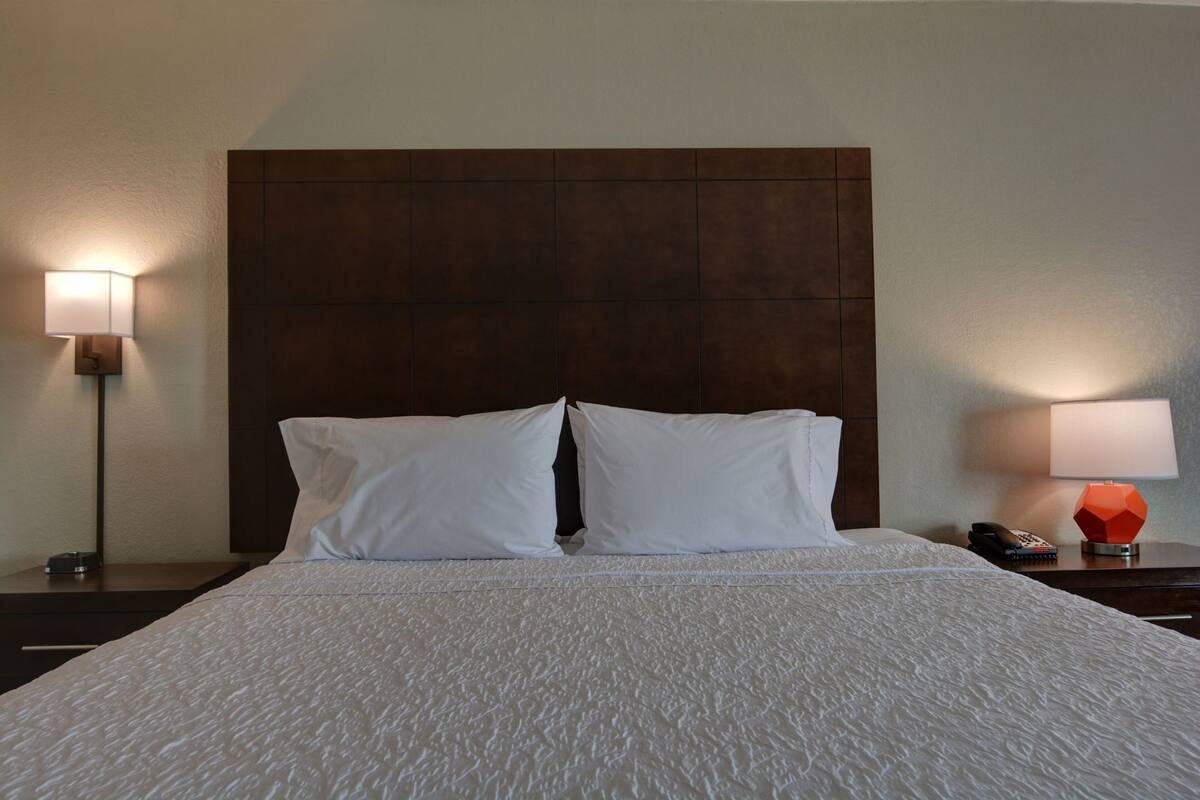 A hotel room with a large bed, two bedside lamps, a nightstand with a phone, and a modern headboard.