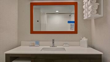 Une salle de bain avec un lavabo blanc, un miroir avec un cadre en bois, un porte-serviettes et des articles de toilette.