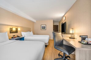 A hotel room with two beds, a desk with a chair, a TV, a phone, and a lamp.