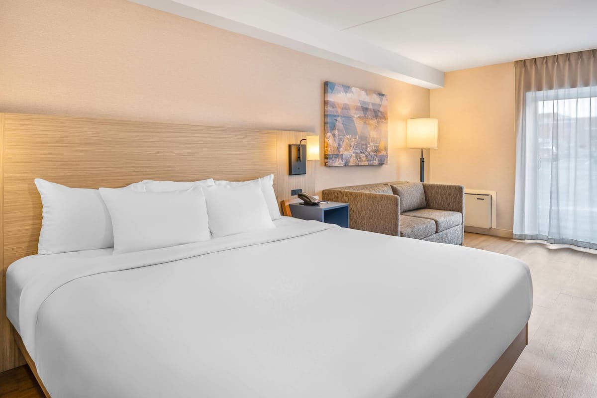 A hotel room with a large bed, a chair, a desk, and a painting on the wall.