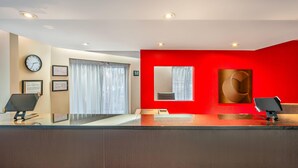 Un espace d’accueil moderne avec un mur d’accent rouge, une horloge, des certificats encadrés et un grand miroir.