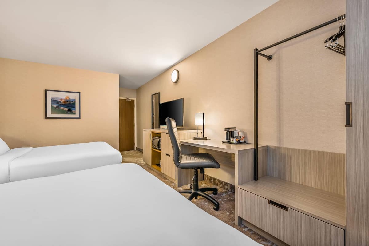 A hotel room with two beds, a desk with a chair, a shower, and a framed picture on the wall.