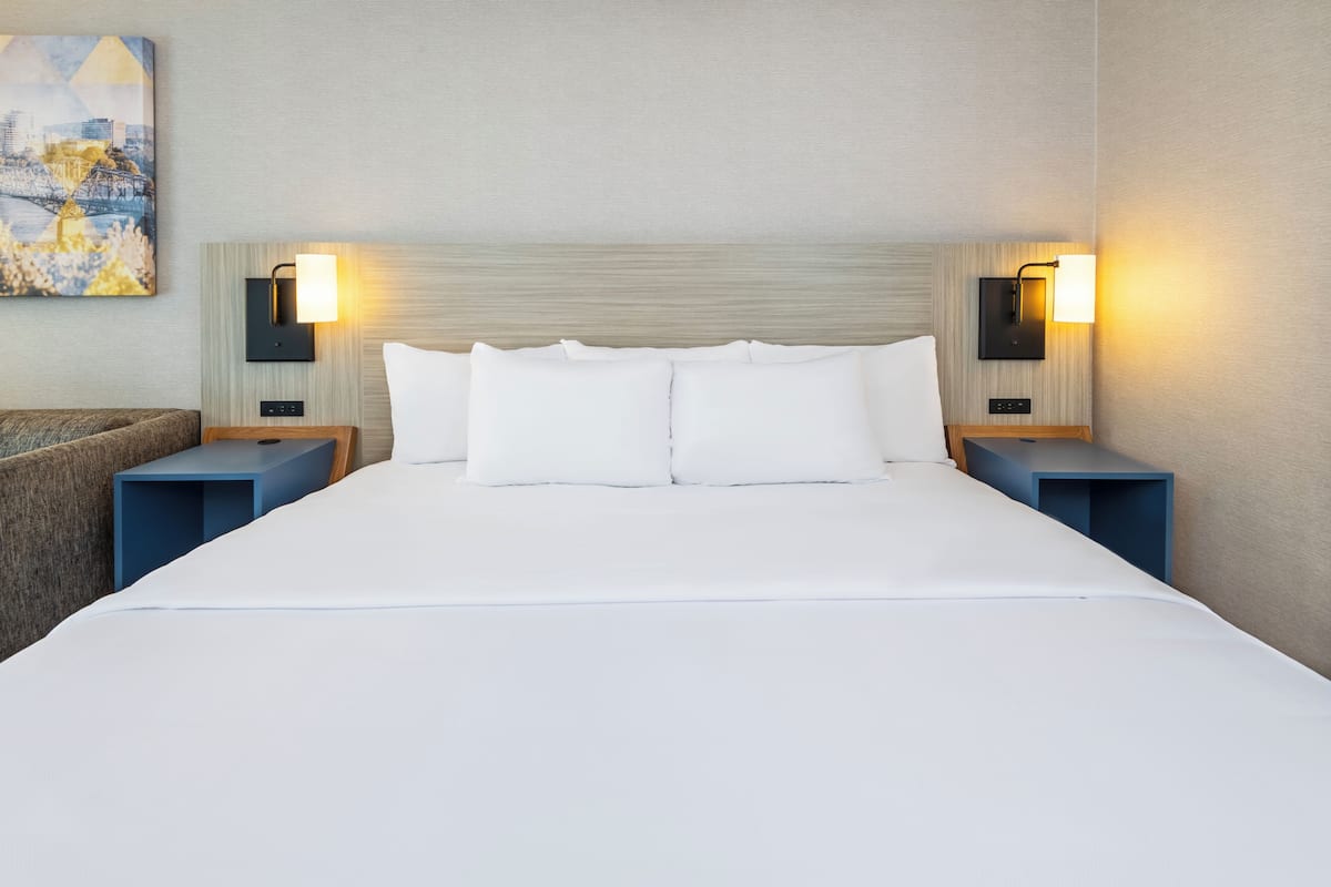 A hotel room with a large bed, two bedside tables, and wall-mounted lamps.