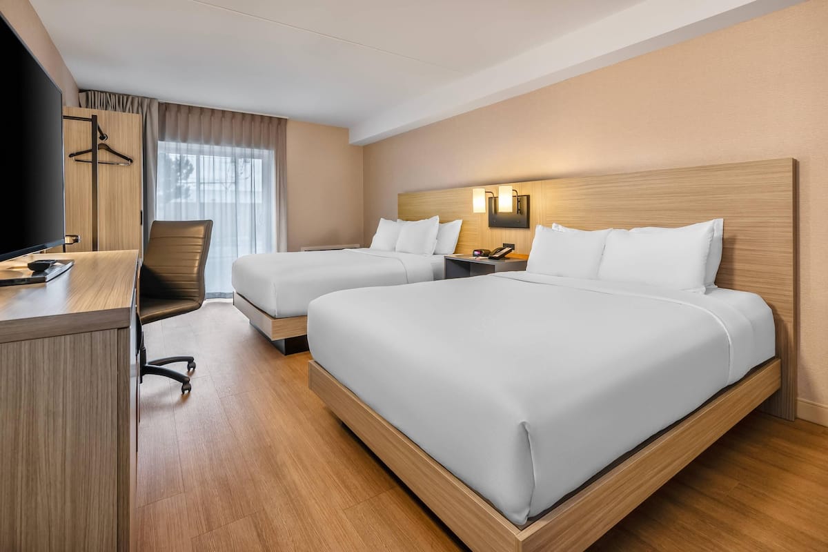A hotel room with two beds, a desk, a chair, and a TV.