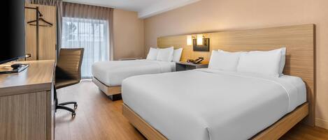 A hotel room with two beds, a desk, a chair, and a TV.