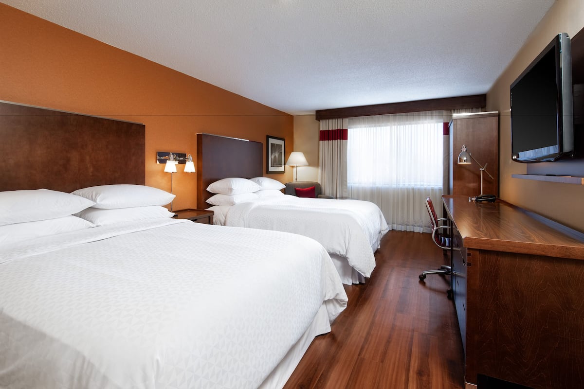 A hotel room with three beds, a desk, a TV, and a window with curtains.