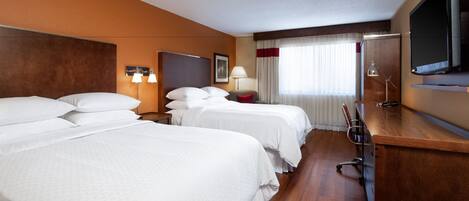 A hotel room with three beds, a desk, a TV, and a window with curtains.