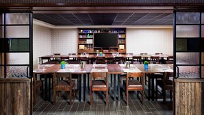 A restaurant with multiple wooden tables and chairs, a large screen, and shelves with various items. - Four Points by Sheraton Edmundston Hotel & Conference Center (Edmundston)