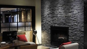A modern living room with a stone wall, a fireplace, and a dining area with chairs and a table. - Four Points by Sheraton Edmundston Hotel & Conference Center (Edmundston)