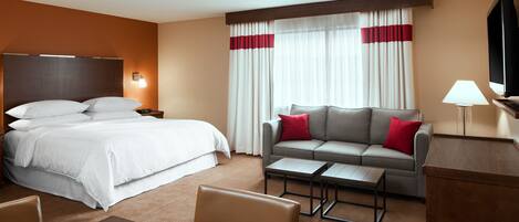 Habitación de hotel con cama, sofá, mesa de centro, televisión y escritorio.