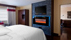 A hotel room with a large bed, a flat-screen TV mounted on a brick wall, a fireplace, and a wooden wardrobe. - Four Points by Sheraton Edmundston Hotel & Conference Center (Edmundston)