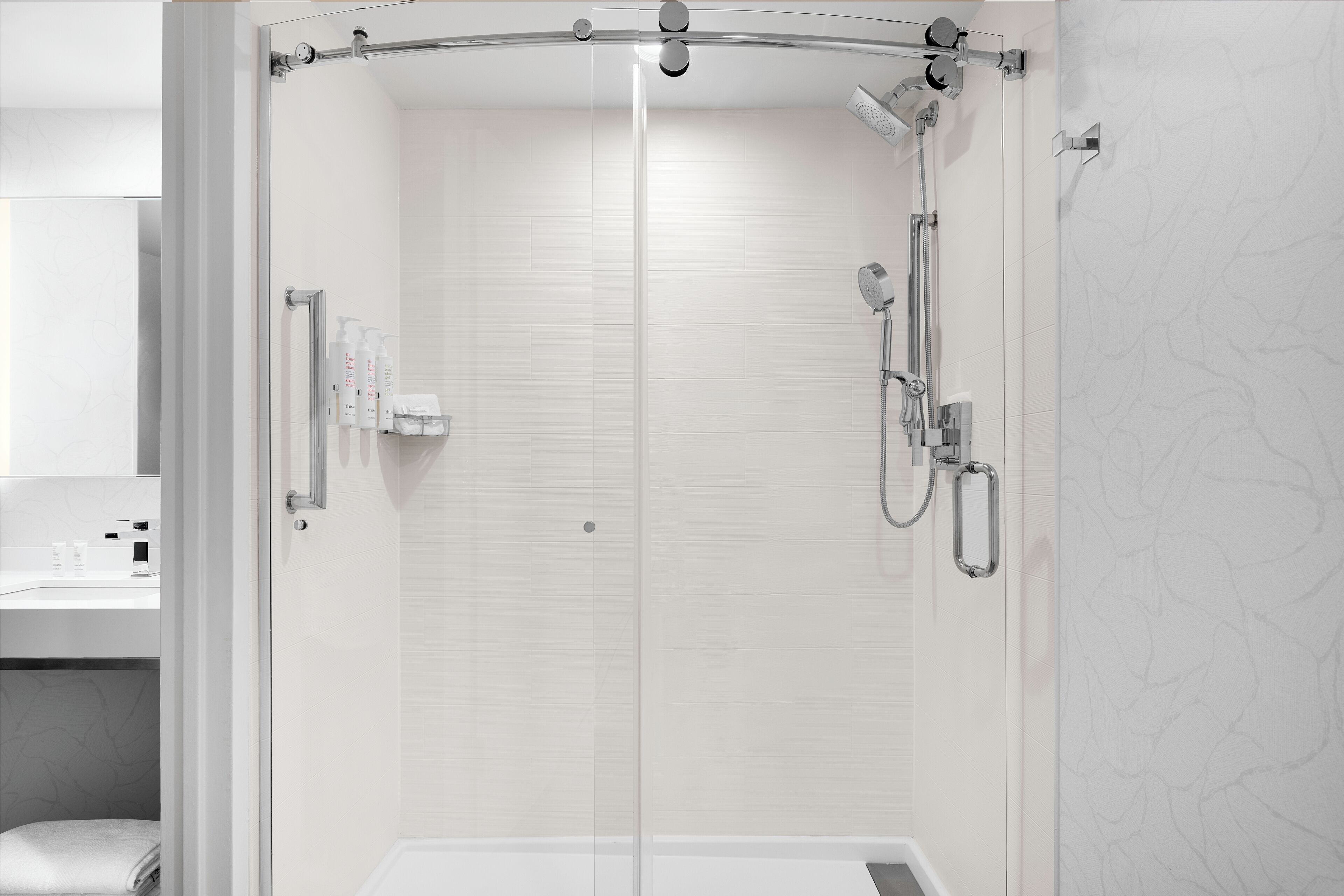 Un bany modern amb dutxa de vidre, un lavabo blanc i una paret amb disseny de marbre.