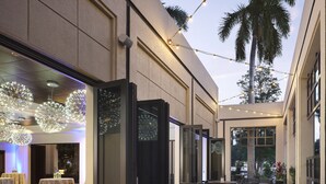 Ein Terrassenbereich im Freien mit runden Tischen und Stühlen, Lichterketten und einer Palme.