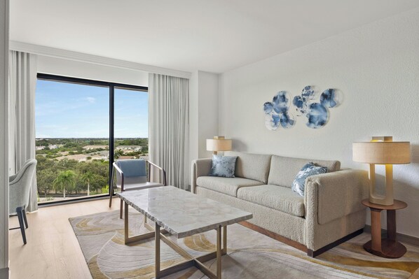 A modern living room with a sofa, two armchairs, a coffee table, and a view of a cityscape through large windows.
