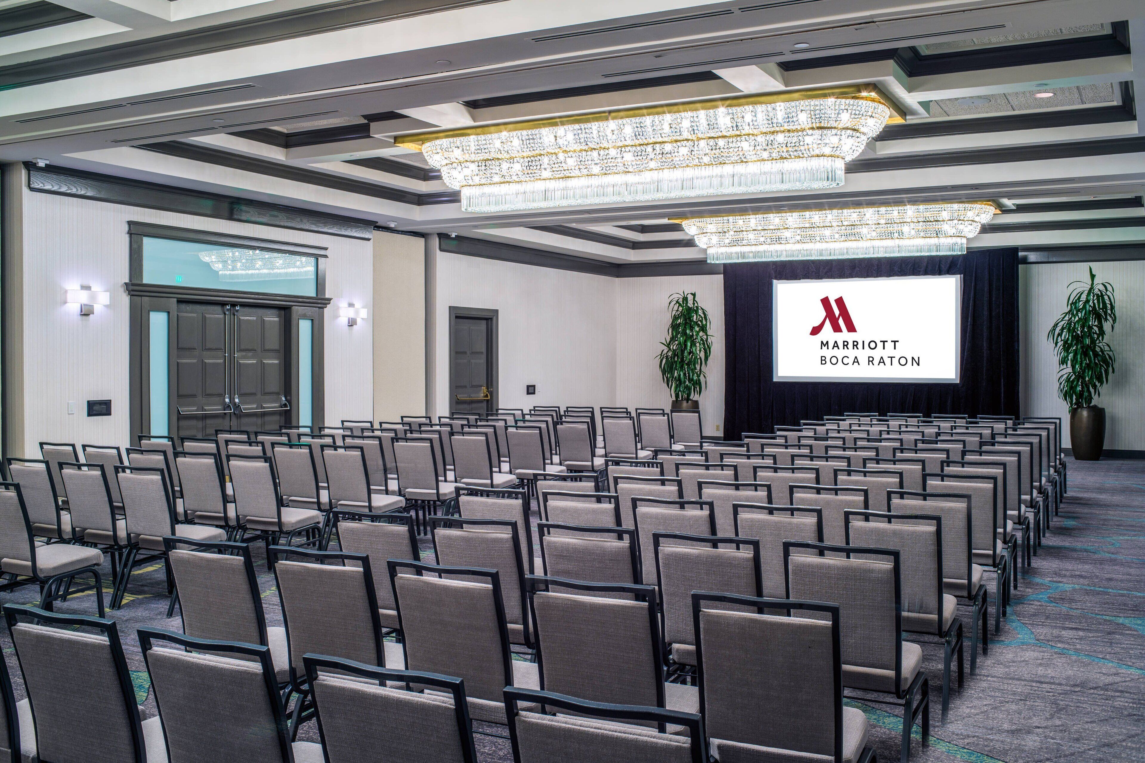 A conference room with rows of chairs, a large chandelier, and a screen displaying the Marriott logo.