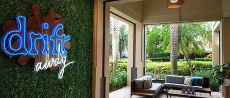 A modern interior with a neon sign reading "drift away," a sofa set, and a view of a lush garden through large windows.