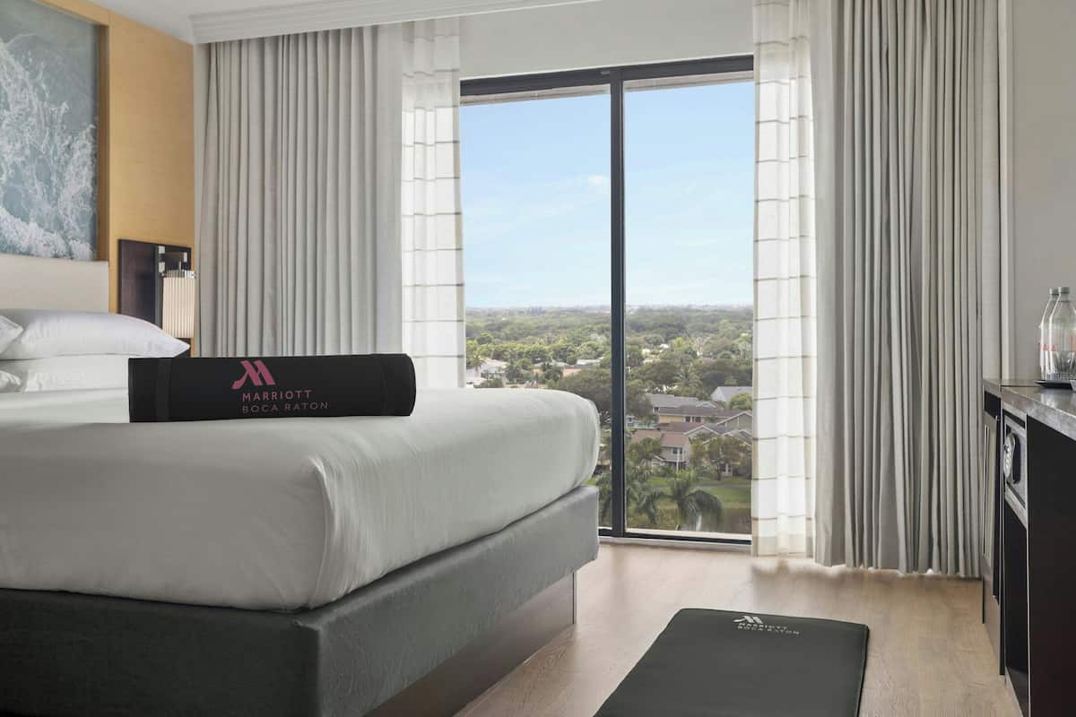 A hotel room with a large bed, a view of the city, and a desk with a chair.