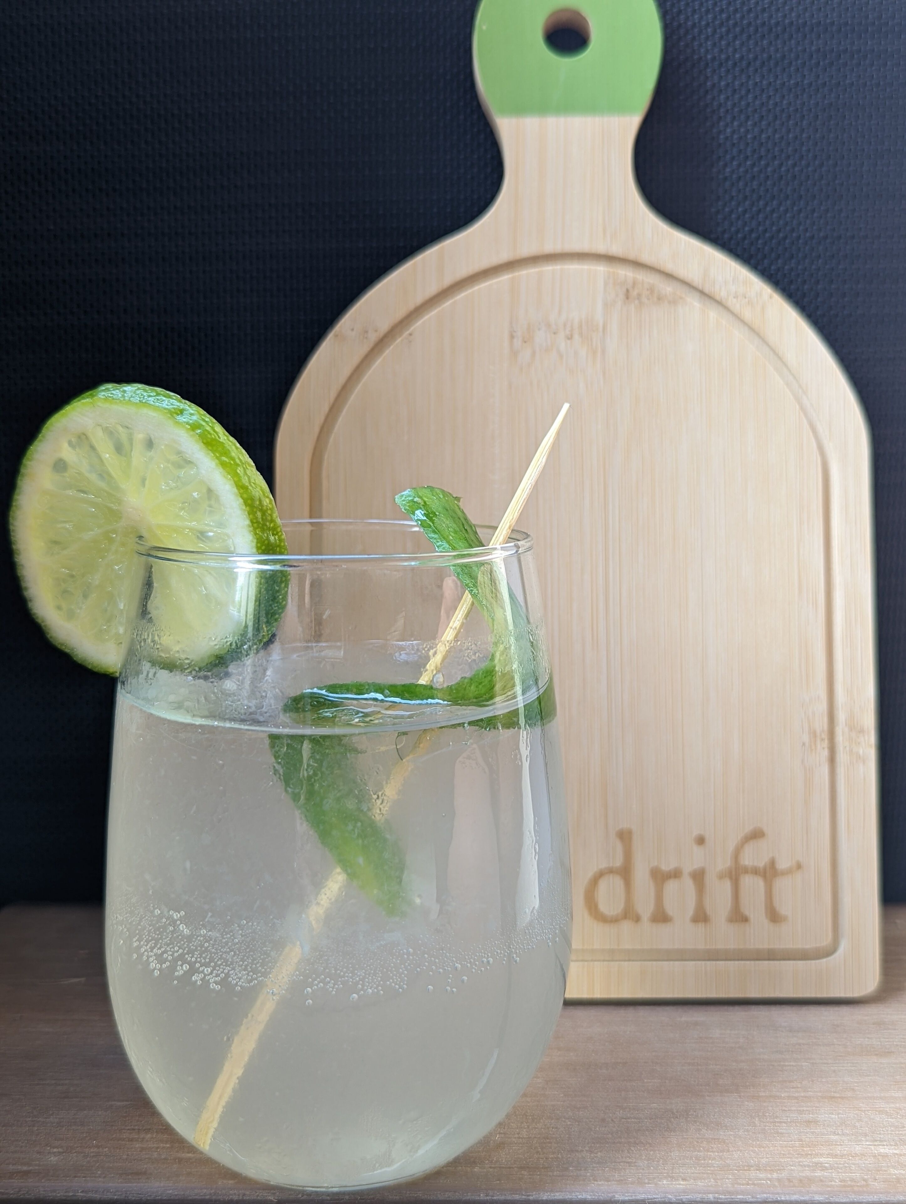 Ett genomskinligt glas med en limeskiva och mynta, placerat på en träyta. I bakgrunden syns en skärbräda med ordet ”drift” skrivet på.