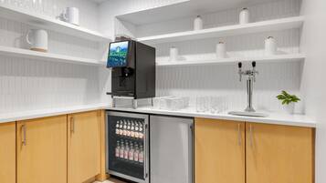 Eine moderne Küche mit weißen Schränken, einer integrierten Kaffeemaschine, einem Kühlschrank und einer Kaffeestation mit Tassen und einer Pflanze.
