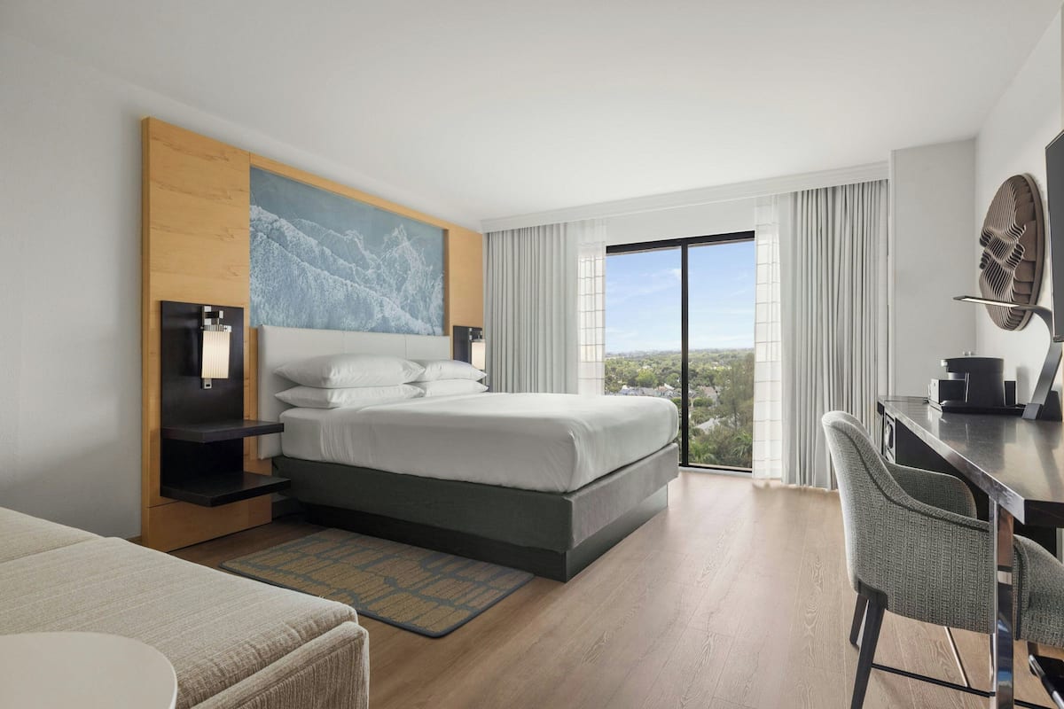 A modern hotel room with a large bed, a desk, and a view of the city.