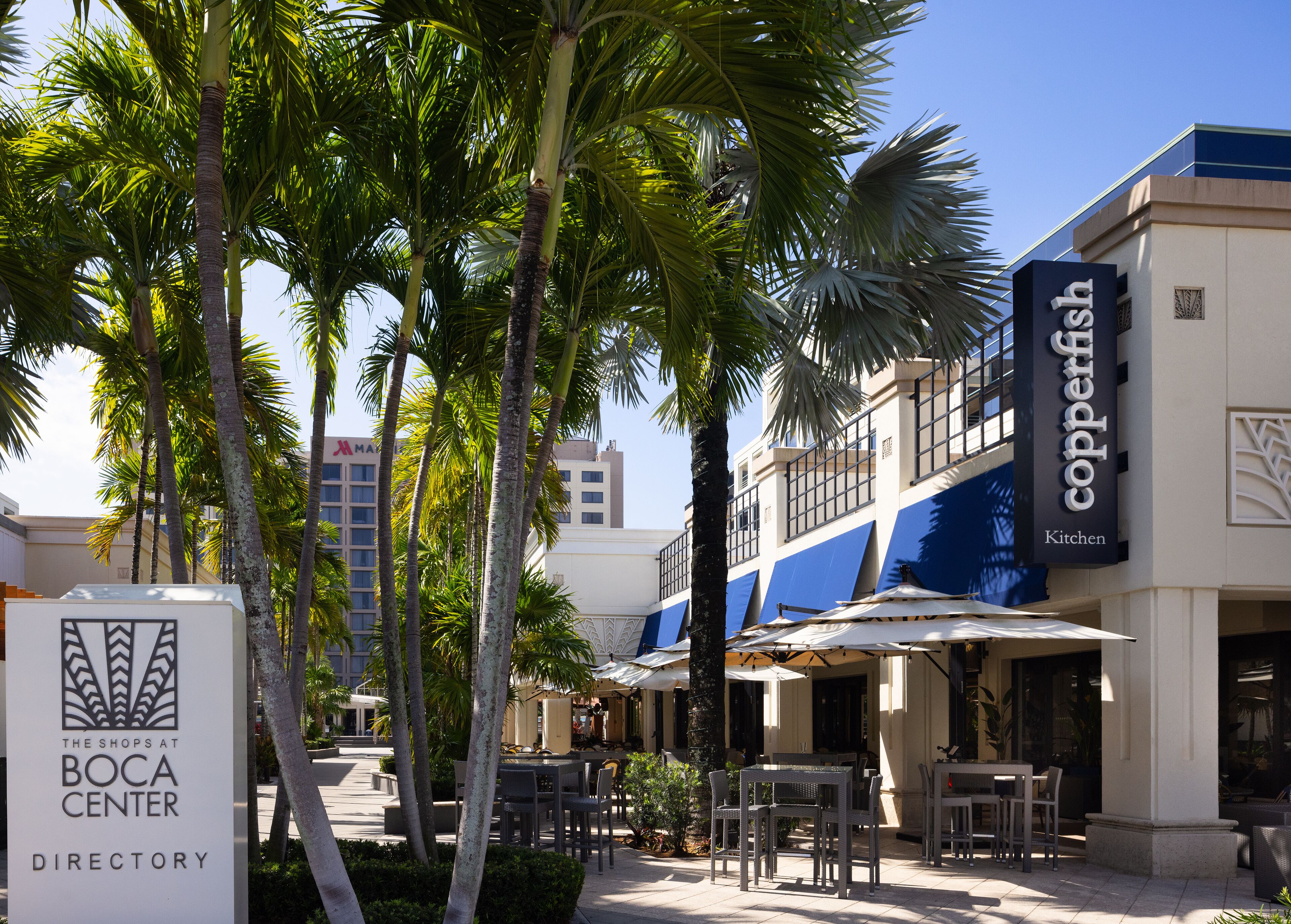 A commercial area with outdoor seating, palm trees, and a building labeled "Copperfish Kitchen".