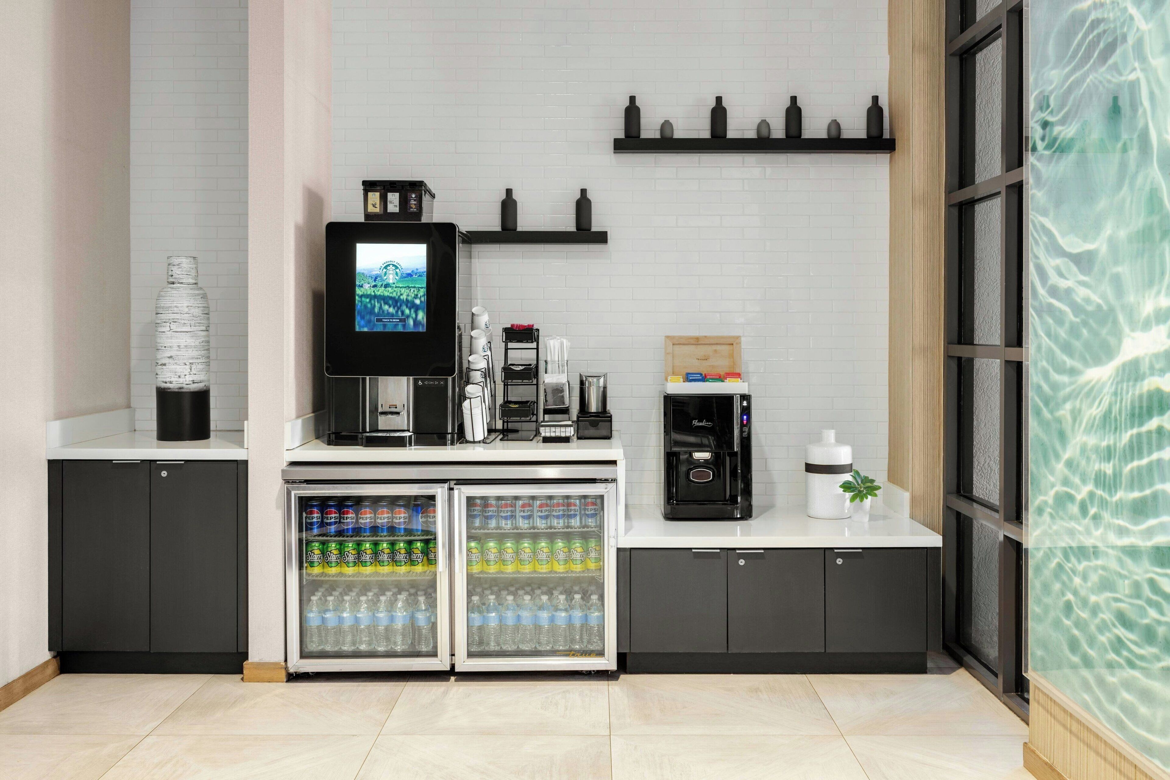 A modern kitchenette with a coffee machine, a TV, and a refrigerator stocked with beverages.
