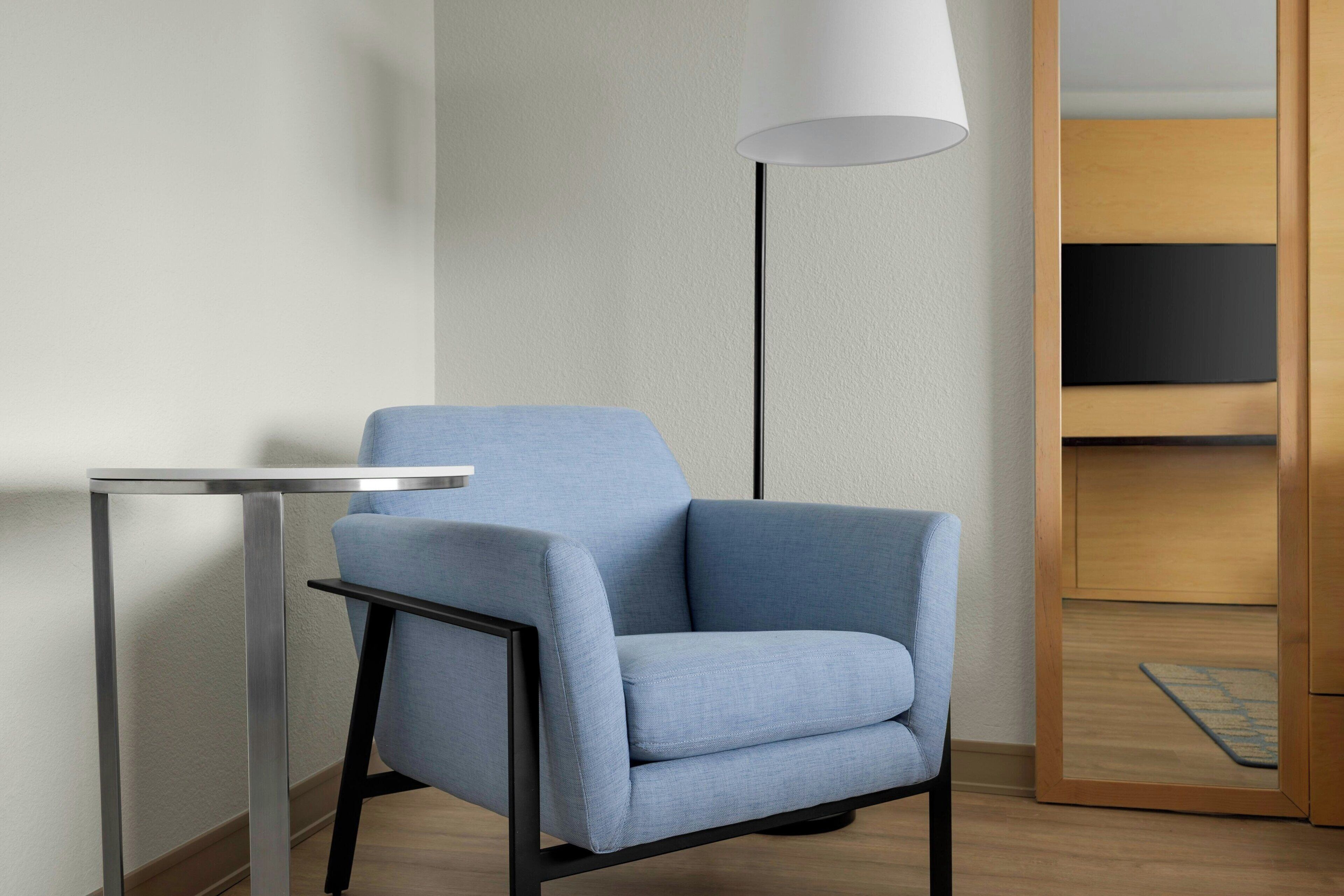 A modern room with a blue armchair, a small table, a floor lamp, and a wooden cabinet.