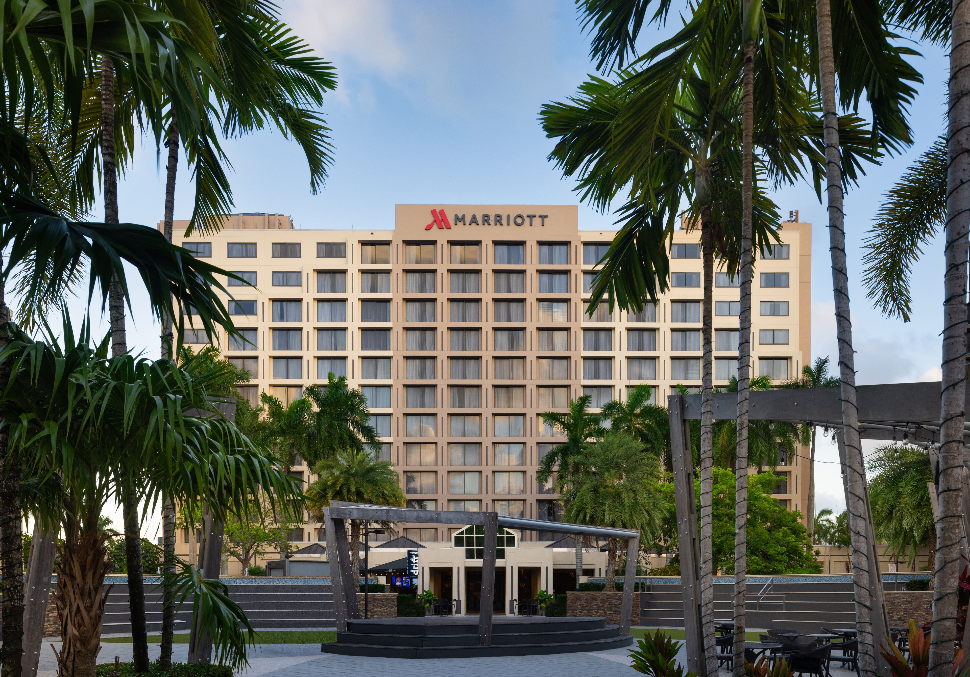 A Marriott hotel with a modern facade, surrounded by palm trees and a covered outdoor seating area.
