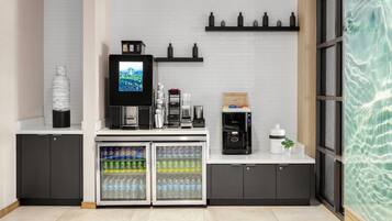 Un área de cocina moderna con cafetera, un refrigerador con bebidas y un televisor mostrando un paisaje.