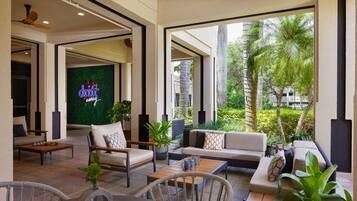A modern outdoor lounge area with seating and a neon sign reading "drinks away".